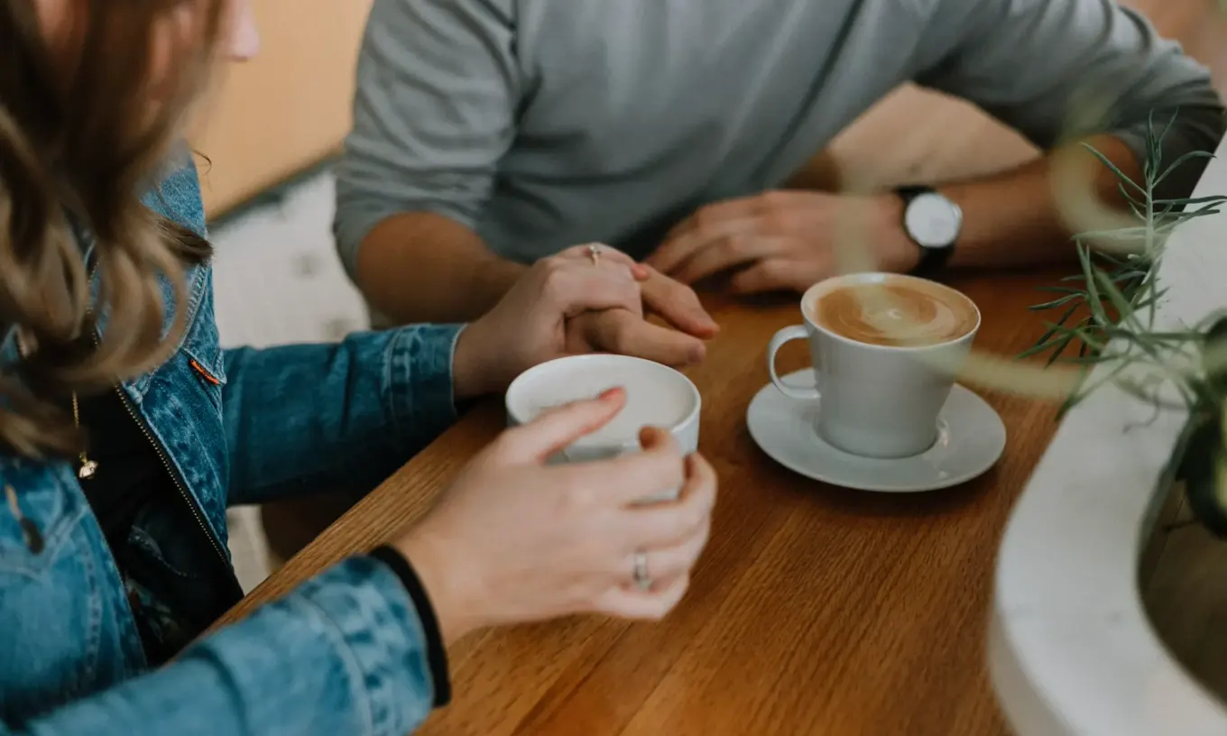 Deux personnes assises face à face autour d'un café, mains posées sur la table